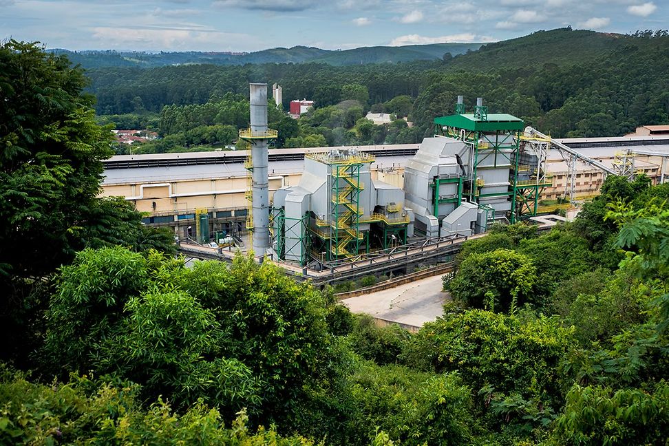 A factory facility nestled in a green, hilly landscape.