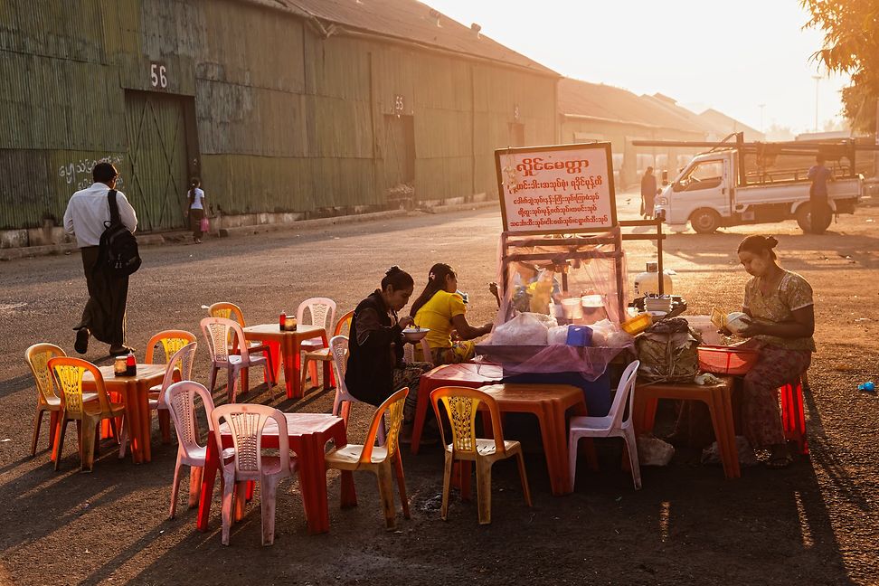 A diverse group of people is sitting on plastic chair having dinner in the lime light from plastic tables