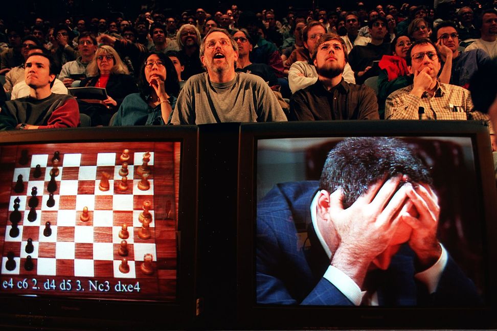 A screen shows a chessboard with a game and a human buried with his head in his hands.