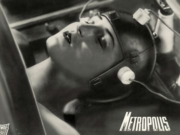 A black and white scene from the movie Metropolis shows a woman's head wearing a helmet with wires attached.