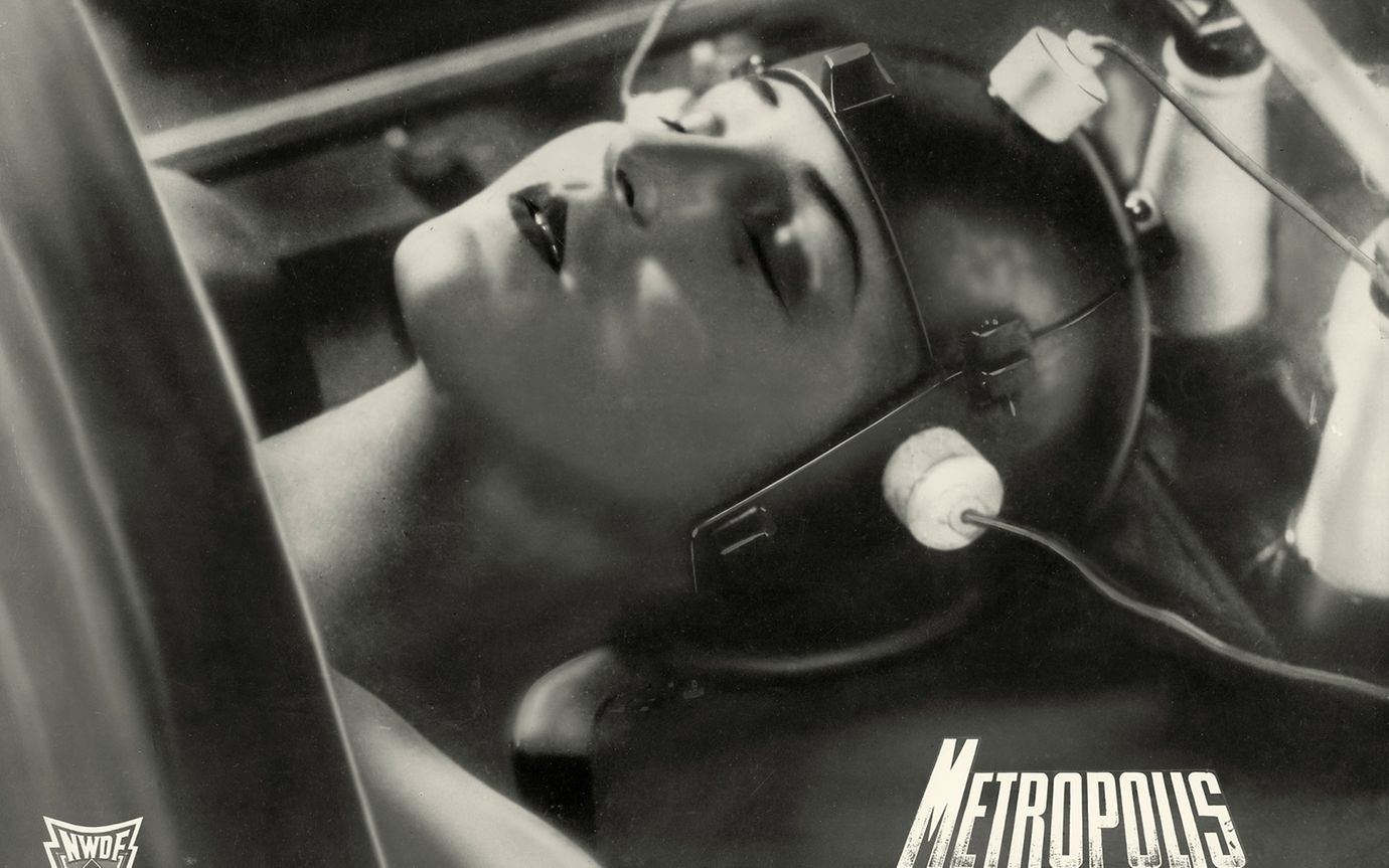 A black and white scene from the movie Metropolis shows a woman's head wearing a helmet with wires attached.