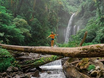 Frau auf einem Baumstamm vor einem Wasserfall